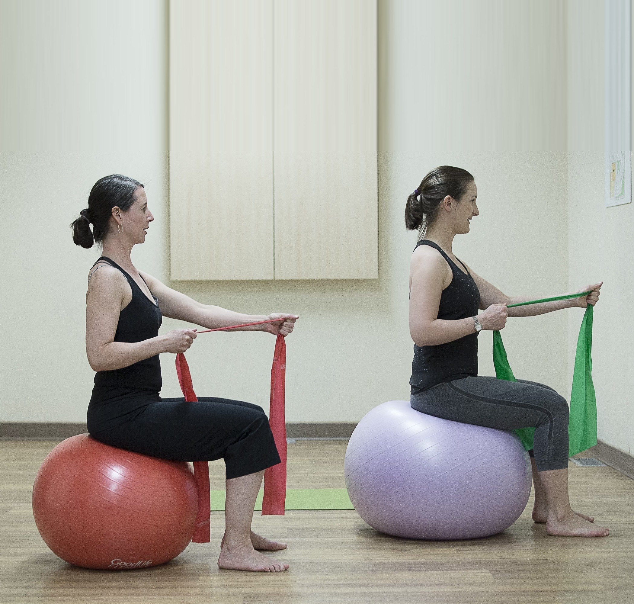 Two women working through a guided resistance-band exercise on stability balls at Optimum Perinatal Health