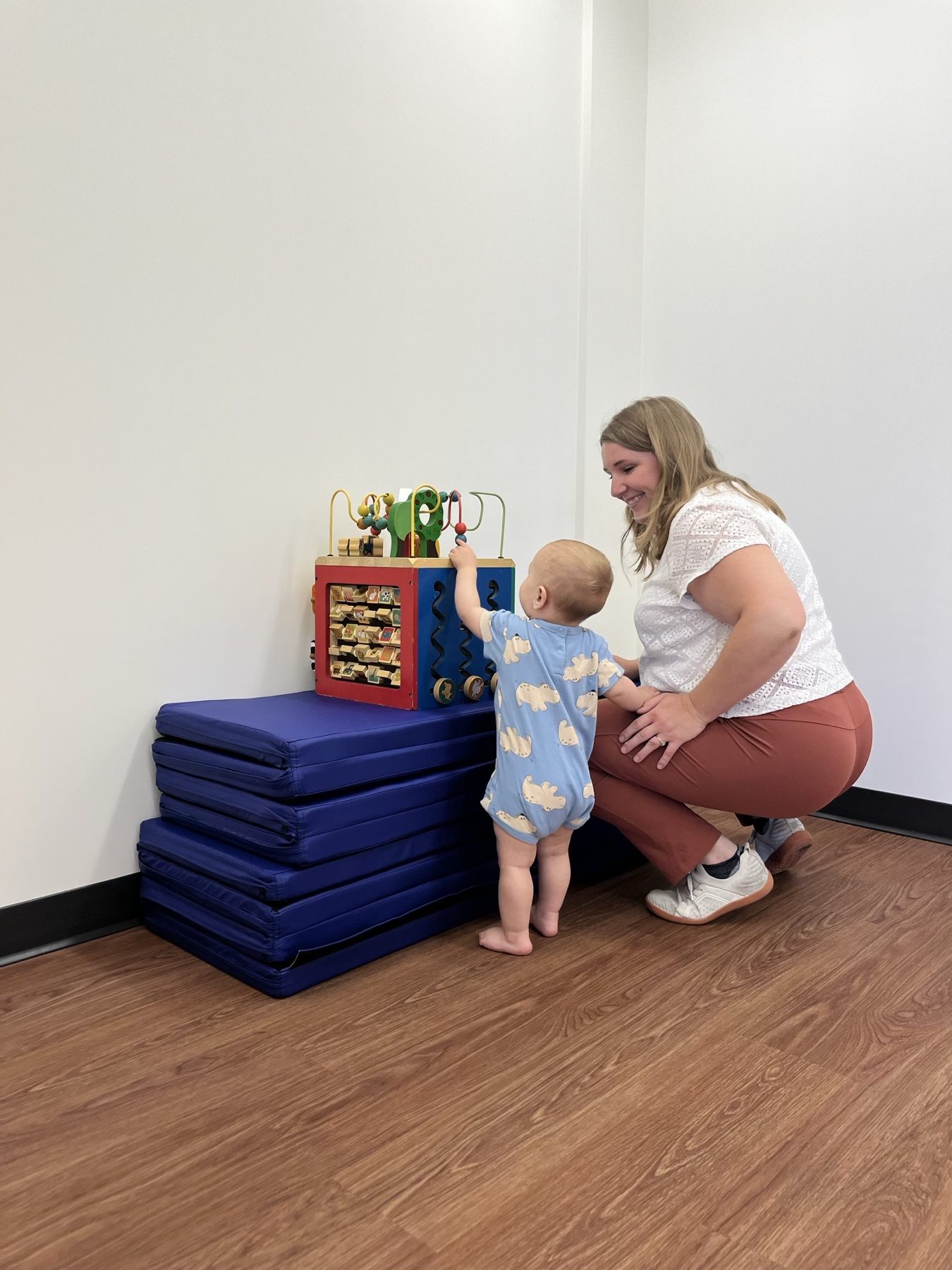 A toddler standing at an activity cube while a physiotherapist supports them