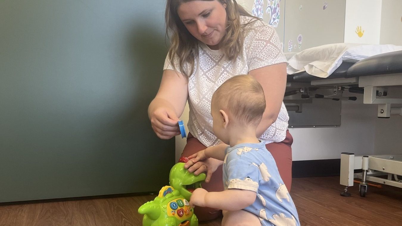 A physiotherapist and a toddler playing together on the floor of a treatment room